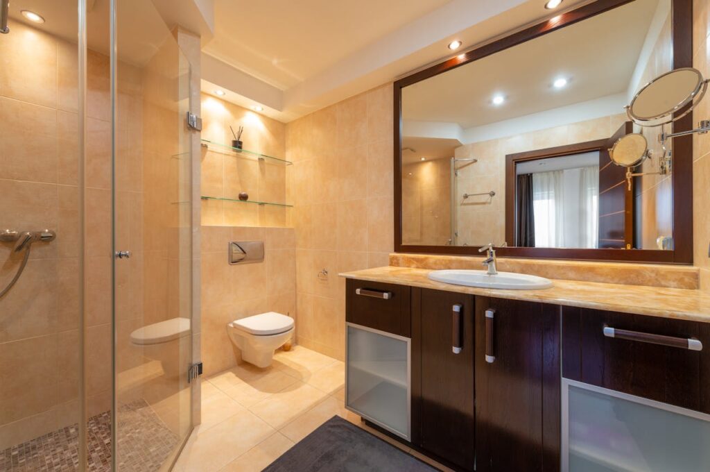 pexels-photo-6956618 Shower room against toilet bowl and cabinet with washbasin under mirrors illuminated by shiny lamps in modern house
